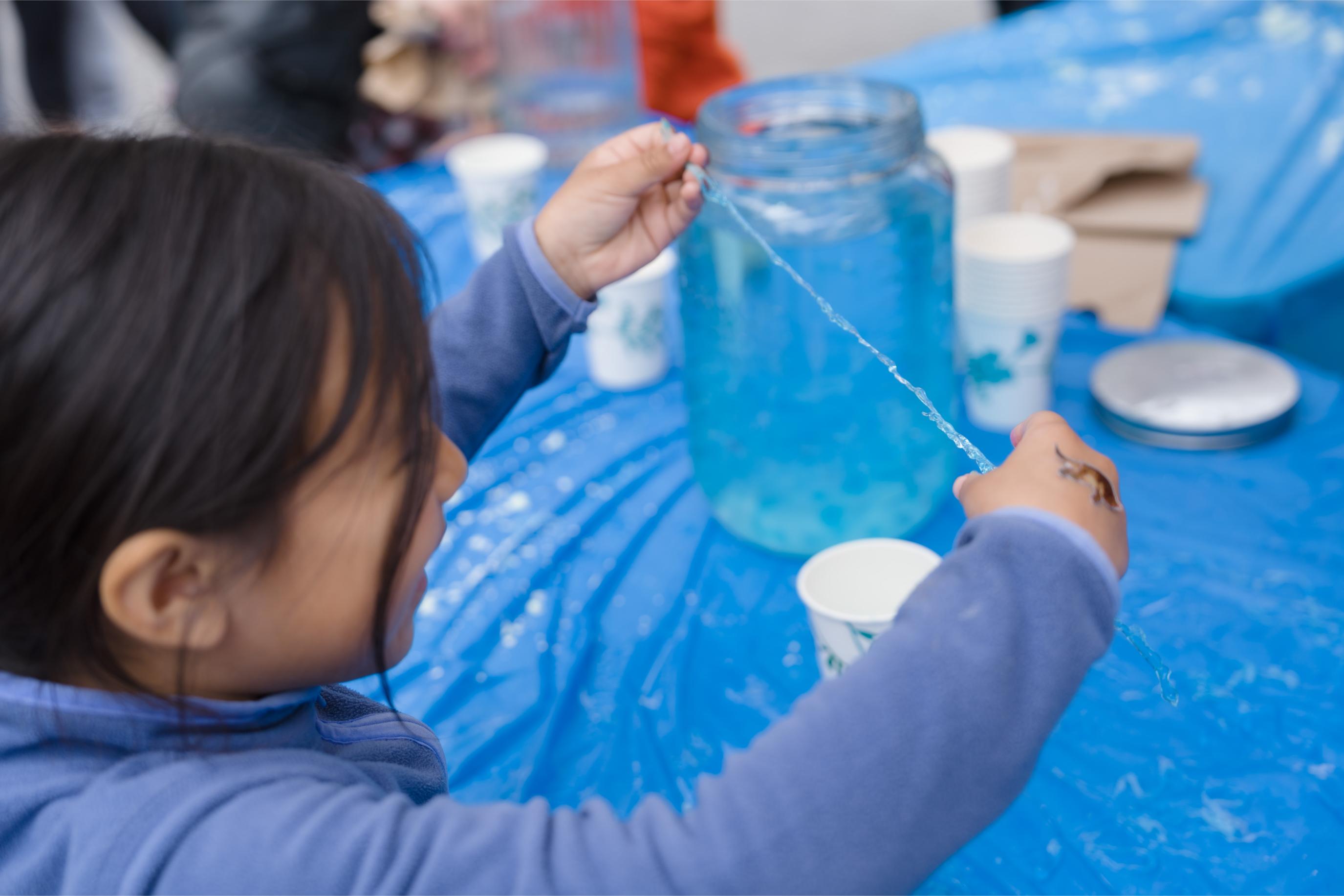 A child is playing with a light blue gel-like substance at the Food Science Now Booth.